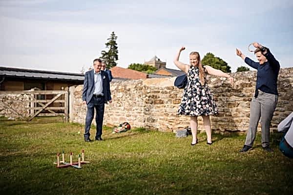 Dodford Manor Wedding Photographer captures a group of people playing a game of croquet in a field.