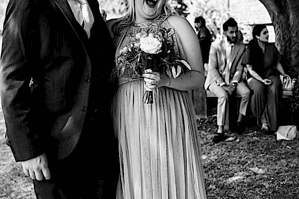 Dodford Manor Wedding Photographer captures a candid moment of a bride and groom laughing in front of a tree.