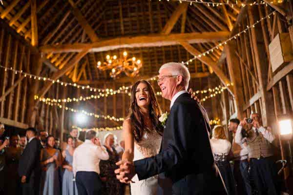 A bride and groom gracefully dance inside a rustic barn, captured by the talented Dodford Manor Wedding Photographer.