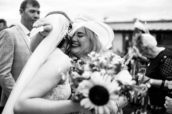 At a Dodford Manor wedding, a bride tightly embraces her bridesmaid in an emotional moment captured by the photographer.