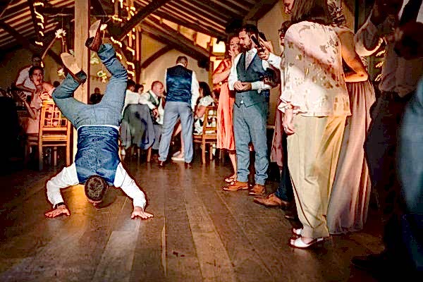 A man, captured by the keen eye of a Dodford Manor Wedding Photographer, gracefully performs a handstand on the dance floor during a joyous wedding reception.