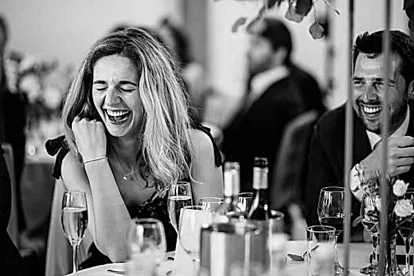 Dodford Manor Wedding Photographer: Black and white photo of a woman laughing at a table.