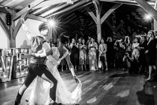 Dodford Manor Wedding Photographer captures a memorable moment of a bride and groom as they elegantly share their first dance in a rustic barn setting.