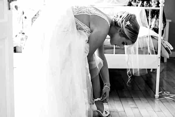 A bride at Dodford Manor putting on her wedding shoes in a bedroom.