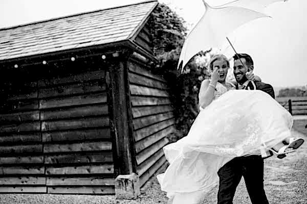 Dodford Manor Wedding Photographer captures a beautiful moment of a bride and groom embracing under an umbrella in the rain.