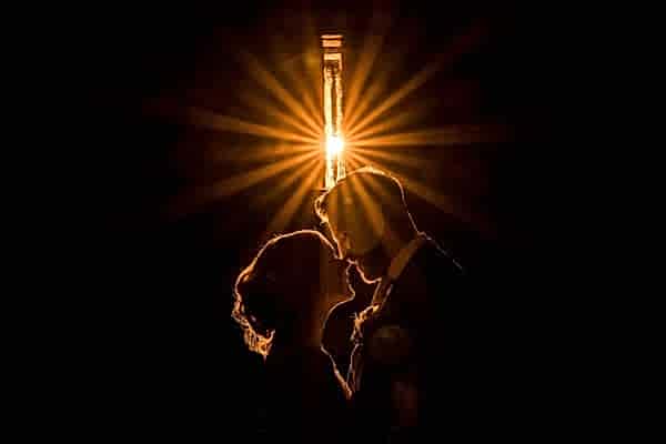 A Dodford Manor Wedding Photographer captures a bride and groom as they are silhouetted against a light bulb.
