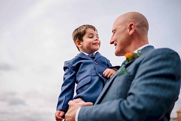 A man in a suit holding a young boy, captured by the Dodford Manor Wedding Photographer.