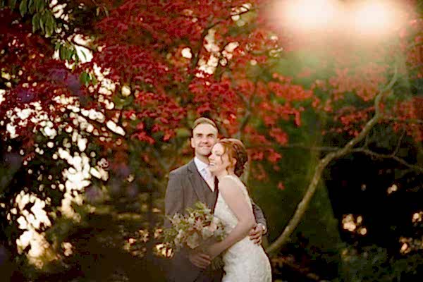 A bride and groom posing in front of a red tree captured by Dodford Manor Wedding Photographer.