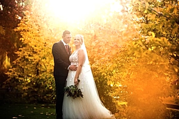 A bride and groom posing in front of autumn trees captured by Dodford Manor Wedding Photographer.
