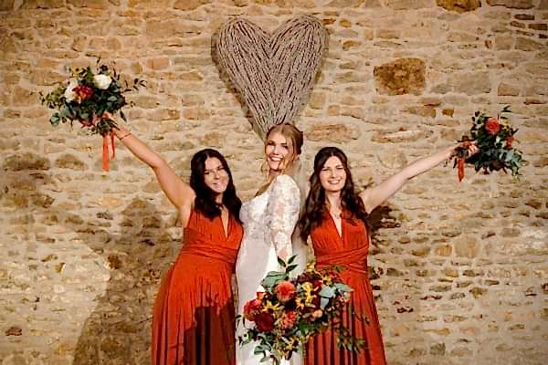 Three bridesmaids holding bouquets at a Dodford Manor wedding, posing elegantly in front of a stone wall.