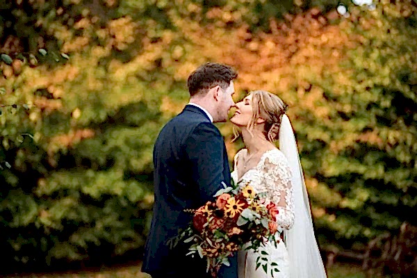 A Dodford Manor Wedding Photographer captures a blissful bride and groom kissing amidst vibrant autumn leaves.