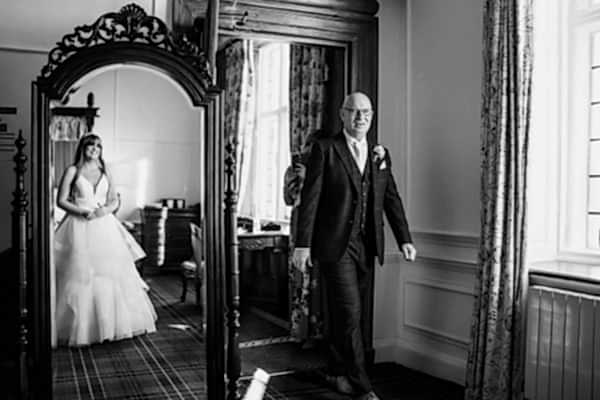 A bride and groom captured by the Dodford Manor Wedding Photographer, standing in front of a mirror.