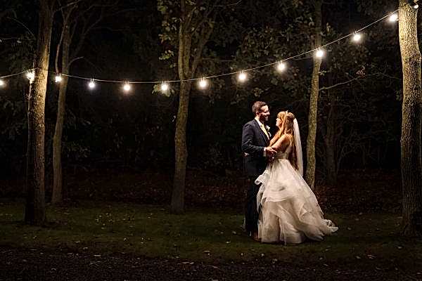 A bride and groom posing romantically under string lights in the woods, captured beautifully by a Dodford Manor Wedding Photographer.