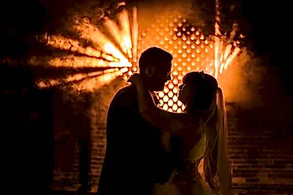 Dodford Manor Wedding Photographer captures a bride and groom standing in front of a brick wall at night, immortalizing their special moment.