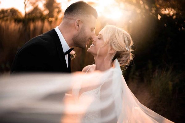 A Dodford Manor Wedding Photographer captures a romantic moment as the bride and groom share a kiss in front of a breathtaking sunset.