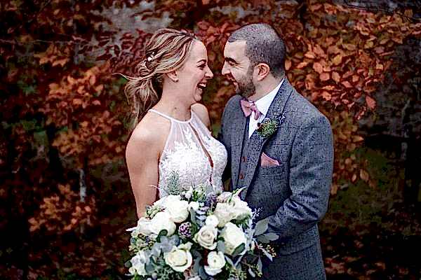 Dodford Manor Wedding Photographer captures the joyful moments of a bride and groom as they smile in front of autumn leaves.