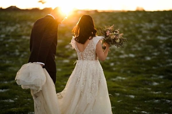 A bride and groom captured by a Dodford Manor Wedding Photographer while walking through a field at sunset.