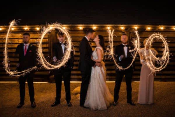 A group of bridesmaids and groomsmen at Dodford Manor Wedding Photographer are holding sparklers and writing 'love'.