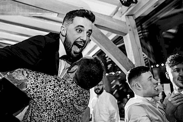 A Dodford Manor wedding photographer captures the heartfelt moment of one man embracing another man on the dance floor.