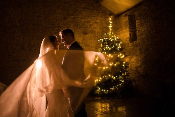 A bride and groom captured beautifully in front of a Christmas tree by a skilled Dodford Manor Wedding Photographer.