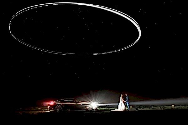 A bride and groom standing in front of a car under a starry sky captured by a Dodford Manor Wedding Photographer.