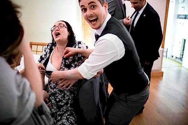 People laughing and unzipping a woman's dress at party.