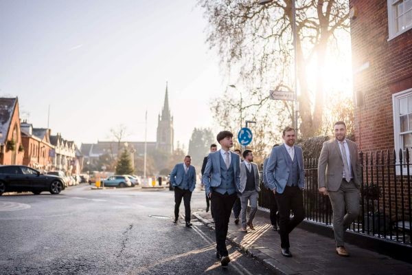 A group of groomsmen walking down a street, captured by Dodford Manor Wedding Photographer.