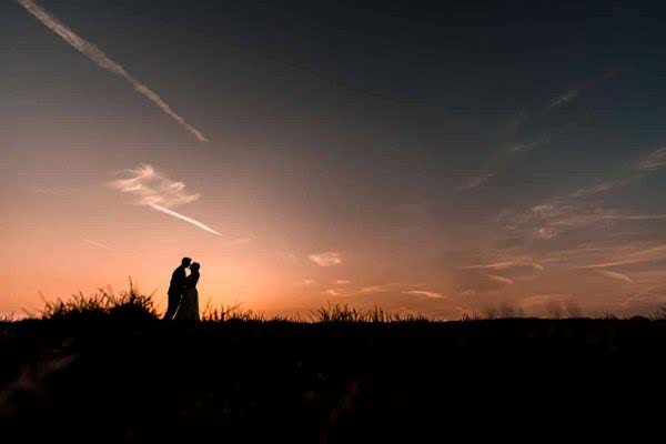 A Dodford Manor Wedding Photographer capturing a silhouette of a couple standing in a field at sunset.