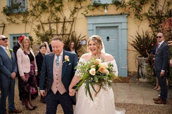 A bride and groom walking down the aisle with confetti thrown at them captured by a Dodford Manor Wedding Photographer.