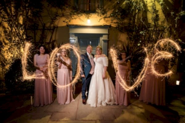 A group of bridesmaids with sparklers in front of a love sign captured by a Dodford Manor Wedding Photographer.