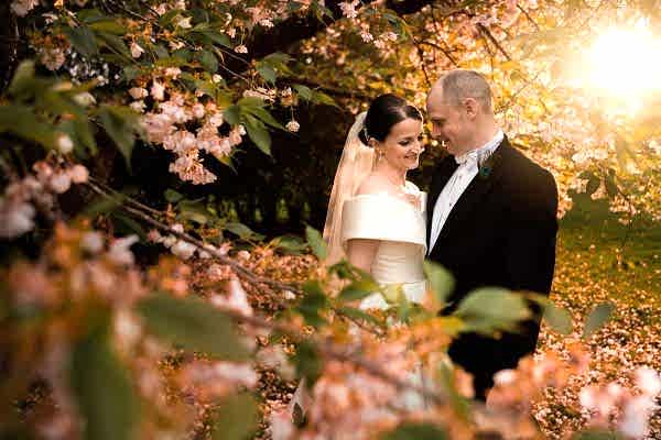 Dodford Manor Wedding Photographer capturing the eternal love between a bride and groom amidst the delicate beauty of a cherry blossom tree.
