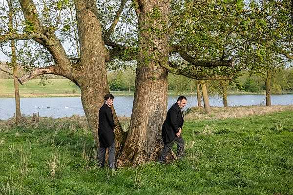 Two men standing next to a tree near a lake, captured by Dodford Manor Wedding Photographer.