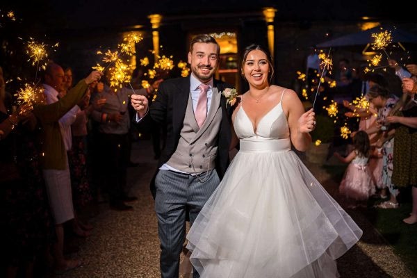 A bride and groom having fun with sparklers during their Dodford Manor wedding captured by a talented photographer.