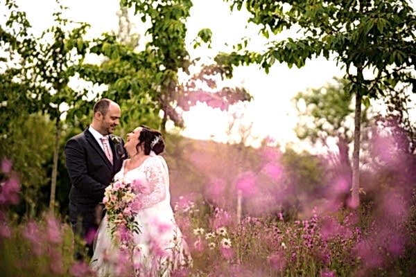 Dodford Manor Wedding Photographer capturing a bride and groom standing in a field of pink flowers.