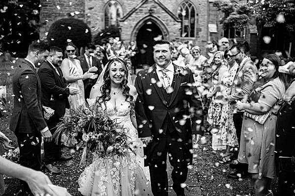 A bride and groom at Dodford Manor walk down the aisle with confetti thrown at them.