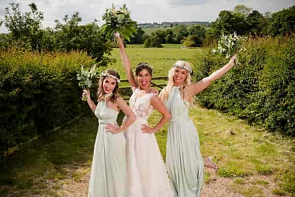 Three bridesmaids posing for a photo in a field captured by Dodford Manor Wedding Photographer.