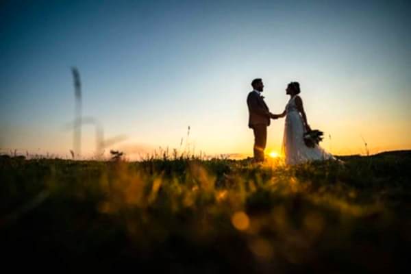 Dodford Manor Wedding Photographer capturing a mesmerizing bride and groom standing in a radiant field at romantic sunset.