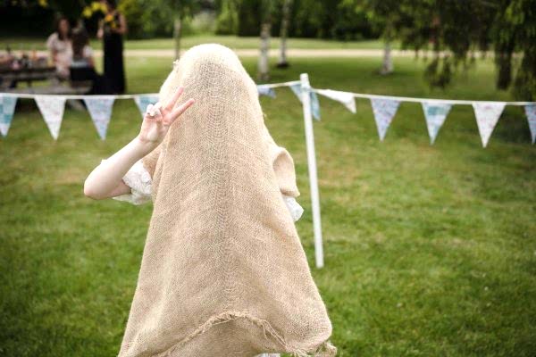 A Dodford Manor Wedding Photographer capturing a girl wearing a burlap cloak in a grassy field.