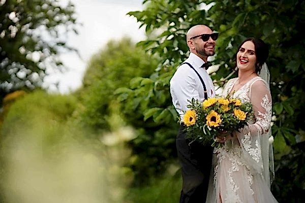 A Dodford Manor Wedding Photographer captures the beautiful moments of a bride and groom standing in a field surrounded by sunflowers.