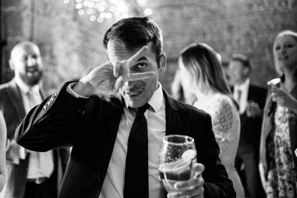 A black and white photo of a man making a face with a glass of beer, captured by the Dodford Manor Wedding Photographer.