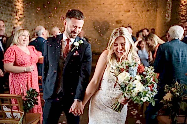 A bride and groom beautifully walk down the aisle at Dodford Manor with confetti joyfully thrown at them.