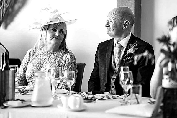 A man and woman sitting at a table with hats on, captured by the Dodford Manor Wedding Photographer.