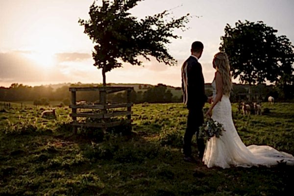 A Dodford Manor Wedding Photographer captures a bride and groom standing in a field at sunset.
