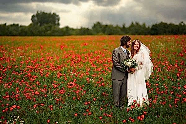 A bride and groom happily posing in a field of red poppies, captured beautifully by the Dodford Manor Wedding Photographer.