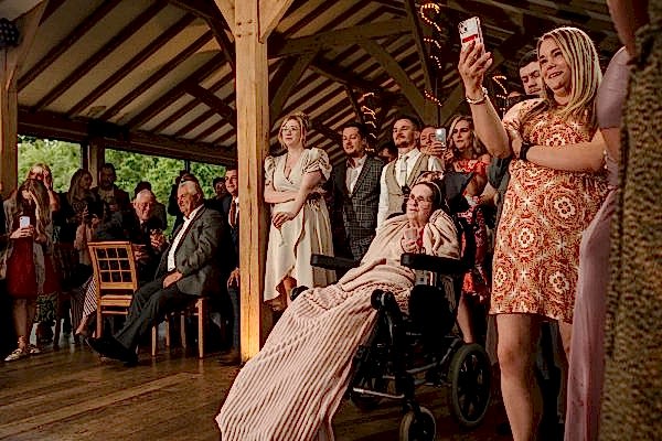 A Dodford Manor wedding photographer captures a woman in a wheelchair taking a picture of the crowd.