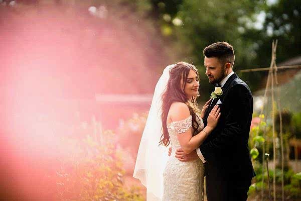 A bride and groom embracing in a garden captured by a Dodford Manor wedding photographer.
