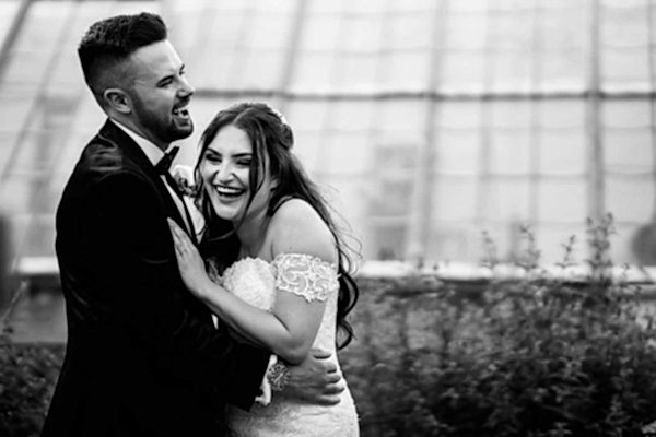 A bride and groom embracing in front of a lush greenhouse, captured beautifully by a skilled Dodford Manor Wedding Photographer.