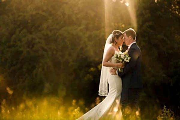 Dodford Manor Wedding Photographer captures a breathtaking moment of a bride and groom kissing in a field at sunset.