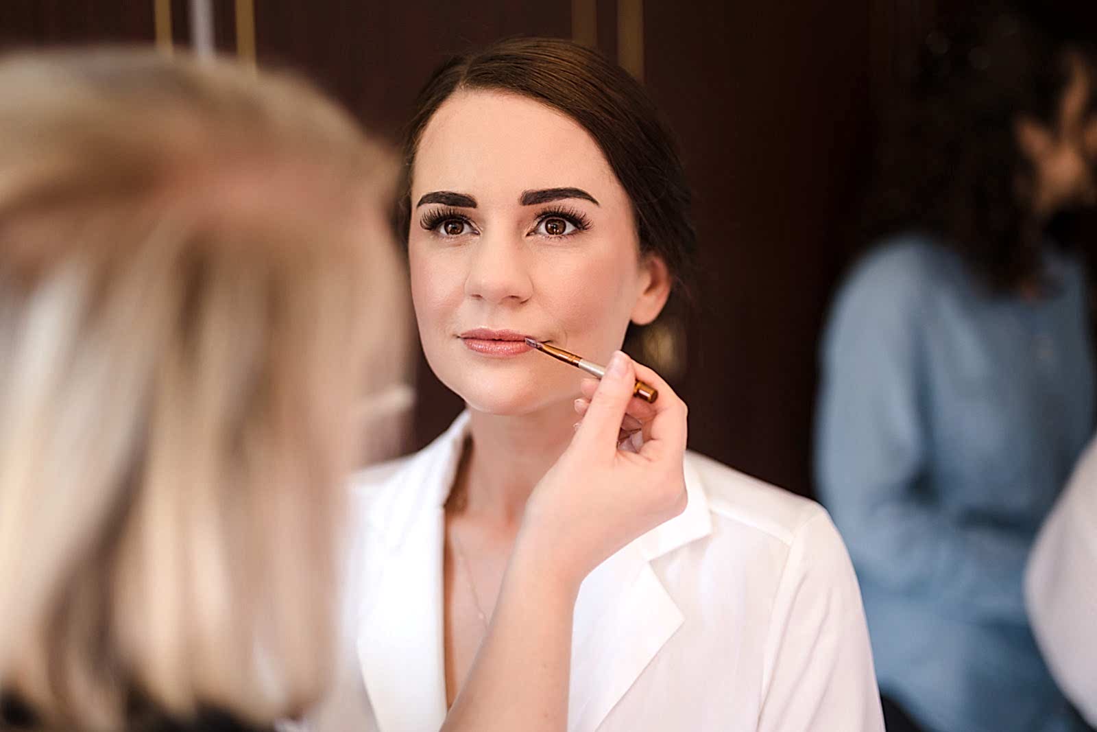 A woman in a white shirt has lipstick applied by another person, captured beautifully by two wedding photographers in Bedfordshire.